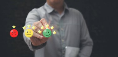 Mutlu gülen yüz simgesine dokunan bir iş adamı, hizmet derecelendirmesinden tatmin olmak için elinde kalem tutuyor. Müşteri hizmetleri ve memnuniyet kavramı çok etkileyici.