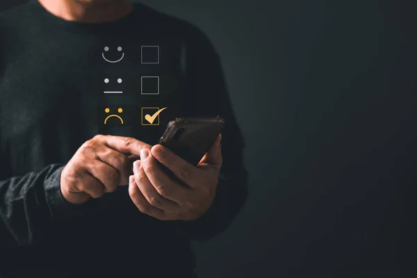 Akıllı telefon kullanan bir adam mutsuz bir müşteri ve üzgün bir surat takınır. Müşteri Deneyimi Memnuniyetsizlik Konsepti, kötü hizmet kötü kalite, düşük not, kötü eleştiri, sosyal medya iyi değil.