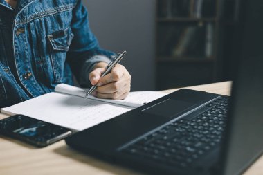 Akıllı telefon kullanan ve planlamada not alan bir adam. Bu da internetteki ödemedir, evdeki oturma odasındaki sandalyeye oturur. Finans ve çevrimiçi alışveriş kavramı.