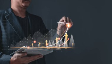 Erkek büyüyen grafikler çizer ve ticaretin ilerlemesini ve mali ve yatırımları analiz eder. Teknolojiyi başarı hedefleri ve büyüyen hisse senetlerine strateji planlamak için kullanın. Çevrimiçi ticaret, ekonomik ve çevrimiçi pazarlama.
