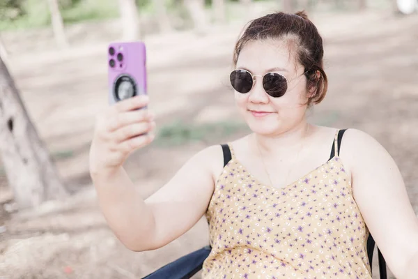 公園でセルフィーを撮って笑顔で暗い眼鏡をかけている女性 — ストック写真