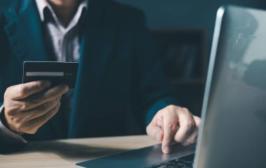İş adamı internet üzerinden ödeme almak veya satın almak için bir bilgisayar dizüstü bilgisayar ve kredi kartı kullanır ve evdeki oturma odasındaki sandalyeye oturur. Finans ve çevrimiçi alışveriş kavramı.
