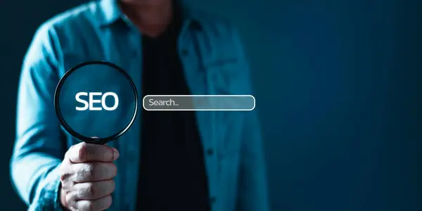Takım elbiseli bir işadamı elinde büyüteçle duruyor. Boş arama çubuğuyla internet bilgilerini tarıyor. Arama Motoru Optimizasyonu SEO Ağ Kavramı.
