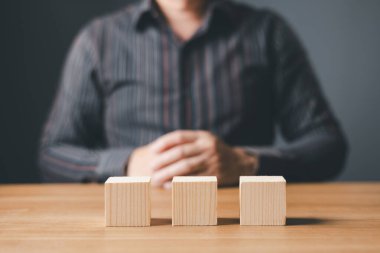 İş adamı, metin veya semboller için kopyalama alanı olan üç blok boş masa ve ahşap üzerinde oturuyor, büyüme başarı süreci için geliştirme kavramı.