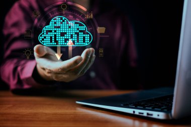 Parlayan bir dijital bulut ikonu ile etkileşim kuran bir işadamı, indirme okları, bulut hesaplama, veri güvenliği ve ağ altyapısını sembolize ediyor. Ahşap masada bir dizüstü bilgisayar duruyor..