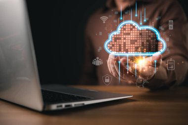 Bir kişi ahşap bir masanın üzerinde parlayan dijital bir bulut tutuyor, yanında bir bilgisayar var, veri depolama, güvenlik ve bağlantı yoluyla yedek ve tutarlılık gibi çözüm kavramlarını sembolize ediyor..