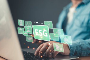 ESG ilkelerini temsil eden, çevresel, sosyal ve yönetimsel sürdürülebilir uygulamaları, etik standartları ve sorumlu yatırımı vurgulayan yüzen yeşil simgeleri olan bir dizüstü bilgisayara yazarlar.