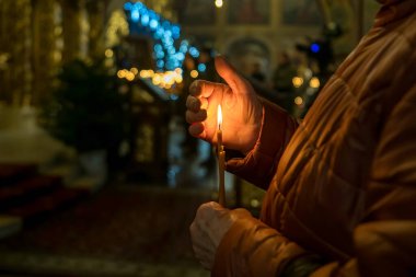 Yaşlı bir kadının elleri kilisede yanan bir mumu tutuyor. Yüksek kalite fotoğraf