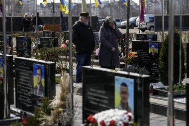 İnsanlar, Bucha 'nın Rus işgalinden kurtuluşunun üçüncü yıldönümünde Kahramanlar Sokağı' na gömülmüş Ukraynalı askerlerin mezarlarına çiçek ve lamba getiriyor. Bucha, Ukrayna, 30 Mart 2025