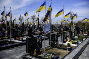 İnsanlar, Bucha 'nın Rus işgalinden kurtuluşunun üçüncü yıldönümünde Kahramanlar Sokağı' na gömülmüş Ukraynalı askerlerin mezarlarına çiçek ve lamba getiriyor. Bucha, Ukrayna, 30 Mart 2025