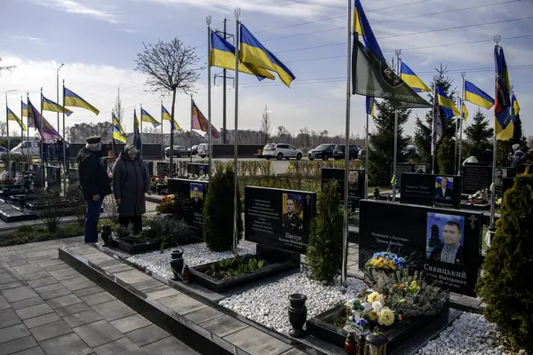 İnsanlar, Bucha 'nın Rus işgalinden kurtuluşunun üçüncü yıldönümünde Kahramanlar Sokağı' na gömülmüş Ukraynalı askerlerin mezarlarına çiçek ve lamba getiriyor. Bucha, Ukrayna, 30 Mart 2025