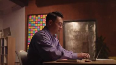 Çalışkan genç bir adam gece saatlerinde şık bir çalışma alanında otururken dikkatle dizüstü bilgisayarına odaklandı.