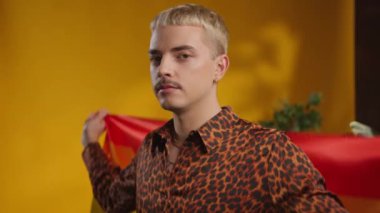 Gülümseyen, beyaz saçlı, şık saçlı, neşeli gurur bayrağı taşıyan genç bir adam.