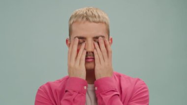 Makyajlı, elleri kameranın önünde olan genç ve ciddi eşcinsel bir adam.