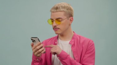 Pembe tişörtlü ve sarı gözlüklü genç adamın kapalı alanda akıllı telefon kullandığı bir stüdyo fotoğrafı.