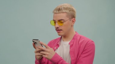 Stüdyoda akıllı telefondan randevu uygulaması kullanarak gülümseyen, makyajlı genç, şık bir gay adam.