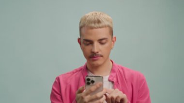 Genç odaklı sarışın eşcinsel adam kapalı alanda akıllı telefon kullanırken sosyal medyada geziniyor.