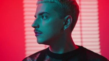 Stüdyoda kameraya bakan makyajlı sarışın genç gay adamın yakın çekimi.