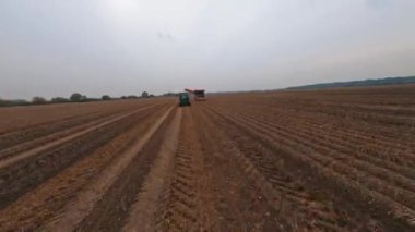 Çiftlik arazisi tarımı. FPV hızlı bir şekilde büyük buğday tarlaları üzerinde uçuyor hasat makineleriyle çayırları ekiyor. Bulutlu bir gün. Kırsal.