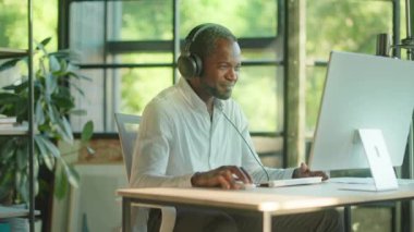 Portre mutlu, çekici, başarılı, Afro-Amerikan erkek işçi gülümseyen bir bilgisayar ve kulaklık kullanıyor. Ofiste sandalyede dans etmek. Yavaş çekim
