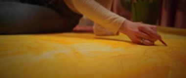 Kırmızı kalemi tutan ve sarı resmin detaylarını çizen kadın ressamın yakın çekimi. Stüdyoda halıya odaklanmış genç bir kadın. Yaratıcılık konsepti. Çalışma süreci. Kapalı