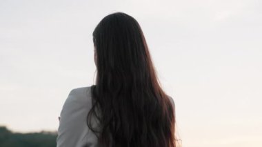 Yakından bakınca çekici genç bir kadın ayakta durup gülümsüyor. Kamera hareket ediyor kızım. Açık havada.