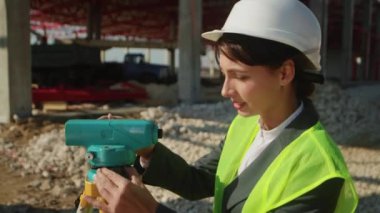 Sarı yelekli ve beyaz şapkalı genç bir kadının yan görüntüleri. Kadın topografçı tüm istasyona bakıyor. İş günü. Sanayi konsepti. Doğruluk. Açık havada.