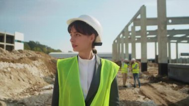 Beyaz koruyucu kasklı genç bir kadının yakın plan portresi inşaat alanının arka planına bakıyor. Kadın topografçı iş başında. Jeodezi uzmanı. İnşaat işi projesi. Açık havada.