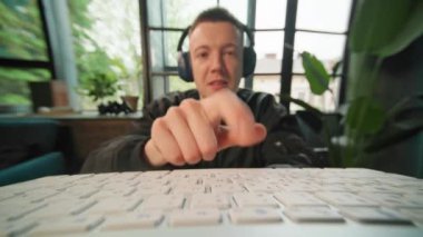 Ön plandaki adam klavyeyle yazı yazıyor. Ofiste bilgisayarla çalışan kulaklıklı, gülümseyen genç bir adam. Pozitif iş adamının portresi