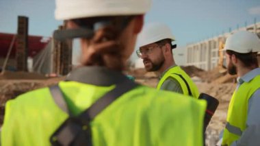 Mühendislerin başındaki adam ölçüm için teodolit gözleme aletini kullanıyor. Grup ayakta projeden bahsediyor. İnşaat şirketi