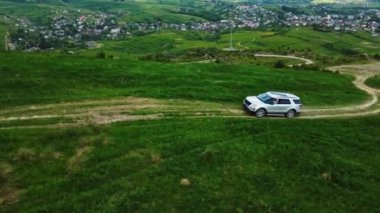 Yeşil tepeler ormanlarıyla çevrili kırsal bir yoldaki beyaz dağ arabasının insansız hava aracı manzarası. Yaz zamanı.