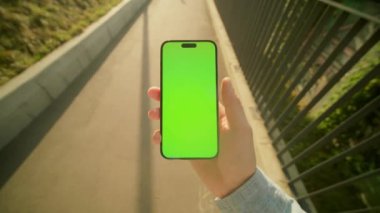 Köprüde yürürken yeşil ekranlı akıllı telefona bakan tanınmayan bir adamın görüntüsü. Bulanık arkaplandaki cep telefonunun ekranındaki erkek el yazısı görüntüsü. Dışarıda.