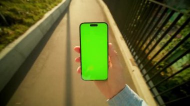 Köprüde yürürken yeşil ekranlı akıllı telefona bakan adamı çekmek. Telefondaki adam doğanın bulanık arka planında mesaj okuyor. Dışarı çıkın. Gündüz