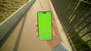 Köprüde yürürken elinde yeşil ekranla cep telefonu tutan tanınmayan bir adamı yakından çek. Bulanık bir geçmişe sahip akıllı telefondan erkek el ile mesajları kontrol etme görüntüsü. Doğa. Yaz zamanı.