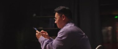 Gözlüklü çekici Asyalı adam cep telefonu kullanıyor. Sosyal medyada sohbet ediyor. Geceleri mutlu oluyor.