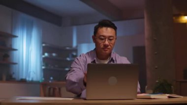 Kapalı dizüstü bilgisayarda oturan Asyalı iş adamının görüntüsü. Gece mesaisi. 360 derece. Kamera hareket ediyor