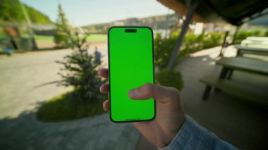 Siyah akıllı telefondan yeşil ekran ile el ele tutuşan adamın görüntüsü. Yazan genç bir adam. Sosyal medyada gezinen adam. Açık havada. Boş zaman konsepti. Kafenin bulanık arkaplanı