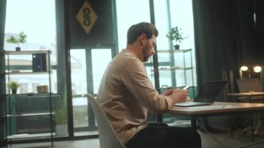 Masada oturan genç adam telefonu ve defteri kullan ve ofiste düşün. Ciddi bir iş adamı. Bilgisayarı açtım. Kamera hareket ediyor. 360 Derece