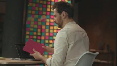 Masada oturan ciddi bir adam dizüstü bilgisayarı kullanarak ofisteki deftere bakar. Kamera hareket ediyor. 360 Derece