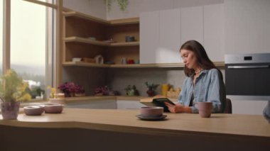 Çekici, kahverengi saçlı, rahat mutfak masasında oturmuş kitap okuyan genç bir kadının görüntüsü. Hafta sonu tatili. Boş zaman konsepti. Dışarıda yağmurlu bir gün