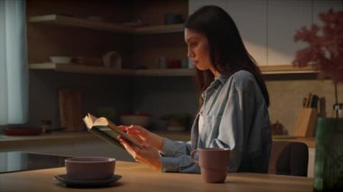 Mutfakta kitap okuyan güzel, zarif, beyaz bir kadın. Uzun saçlı, güzel bir esmerin görüntüsü. Evdeki rahat atmosfer. Öğleden sonra güneş ışığı