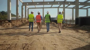 İnşaat alanında iş kıyafetleri içinde yürüyen bir grup inşaatçının arka görüntüleri. Parlak yelekli inşaat işçilerinin birbirine beşlik çakması. Açık havada. İnşaat işi