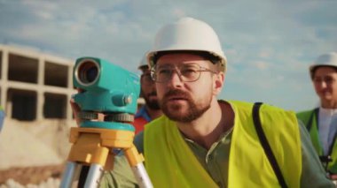 Adam, inşaat projesi hakkında mühendislerle optik seviyelerde konuşuyor. Güneş ışığı altında kask ve üniforma içinde durmak. İnşaat şirketi