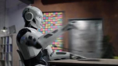 Bilgisayarla masada oturan genç insansı robotun hareketli görüntülerini takip ediyoruz. Android 'in çalışma günü. Serbest meslek kavramı. 360 derece atış. Parallaks etkisi. Hız. Sinematik