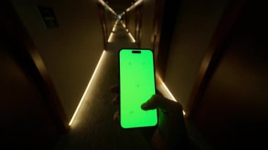 Geceleri koridorda yürüyen tanınmayan genç bir adam. Kapalı alanda inanılmaz ışıklandırma. Beyaz perdeli akıllı telefon kullanan bir adam otelin beyaz kapısını arıyor. Modelleme. Modern iç mimari