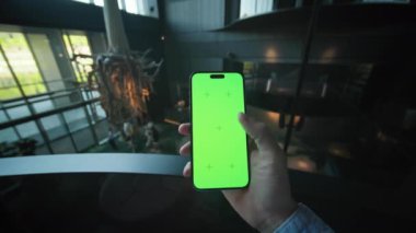 Elinde akıllı telefon olan bir adamın fotoğrafı. Tanımlanamayan bir adamın yeşil ekranlı bir cihaz kullandığı görüntüler. Yakın plan. Modern, güzel aydınlatmalı karanlık salon. Harika bir iç mekan. Kapalı