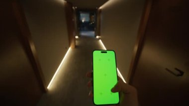 Akıllı telefonlu genç bir adamın, koridordan geçişi, kapıları ve modern aydınlatmayı karanlıkta çekmesi. Yeşil ekran krom anahtarlı cep telefonu kullanan bir adam. Otel
