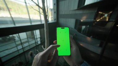 Tanımlanamayan beyaz adamın elleri yeşil ekranlı akıllı telefonu tutuyor ve sosyal medyada geziniyor. Modern iç mekanın arka planında cep telefonu kullanan bir adam. Otel koridorunun ikinci katında. Kapalı