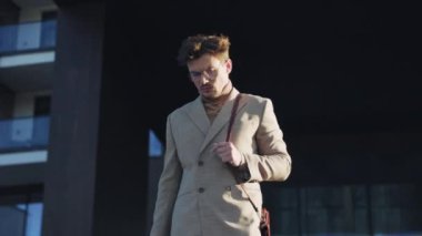 Gözlüklü genç adam güneş ışığında bir şehirde cep telefonuyla konuşuyor. Kendine güvenen genç iş adamları açık hava ticaret bölgesinde konuşuyorlar.