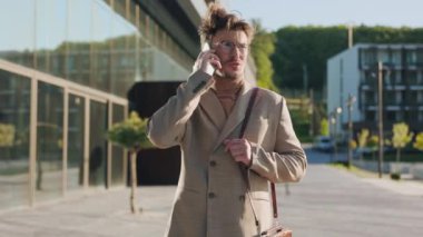 Gözlüklü genç adam güneş ışığında bir şehirde cep telefonuyla konuşuyor. Kendine güvenen genç iş adamları dışarıda sohbet ederler.